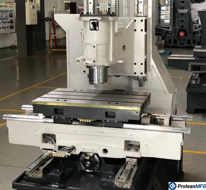 A closeup image of a 3-axis CNC milling machine with spindle, vertical column, and flat worktable, inside an industrial workshop