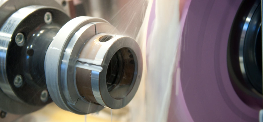 Close up of CNC grinding wheel with abrasive fluid flowing next to cylindrical part