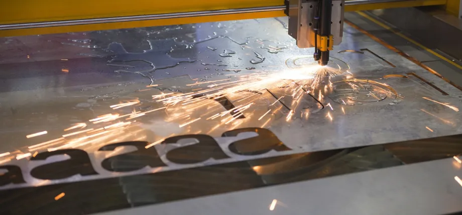 A close-up image of a laser cutting machine in operation, cutting the letter "A" into a metal sheet