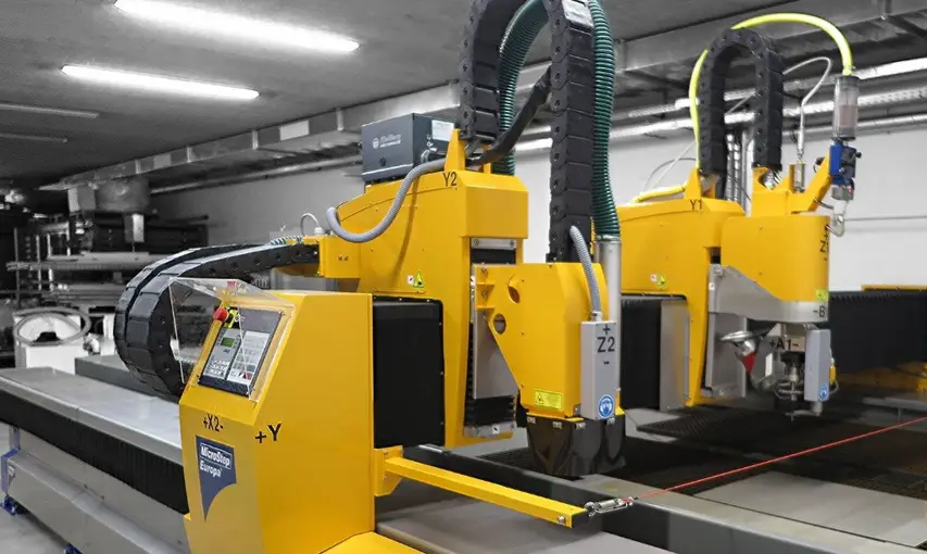 A yellow CNC waterjet cutting machine with two gantry-mounted heads 