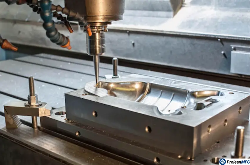 A close-up image of a metal workpiece clamped on a CNC machine table, a 3-axis milling machine creating a mold indentation on the workpiece.
