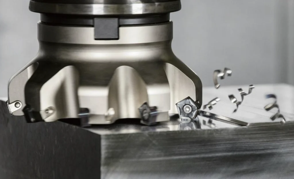 Close-up of face milling operation on a metal part, showing a cutting tool with inserts and metal chips falling off during machining