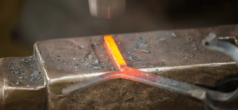 Close up of a yellow hot metal part under a hammer strike