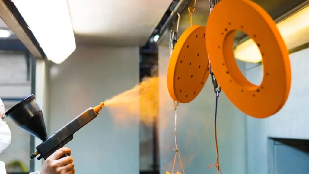 Worker applying orange powder coat to parts.