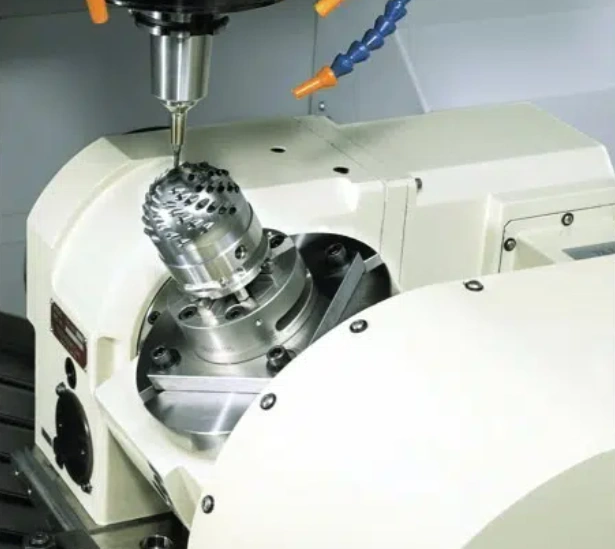 Silvery-gray metal part with a profiled end and multiple holes being machined at an angle on a rotary table 5-axis CNC machine.