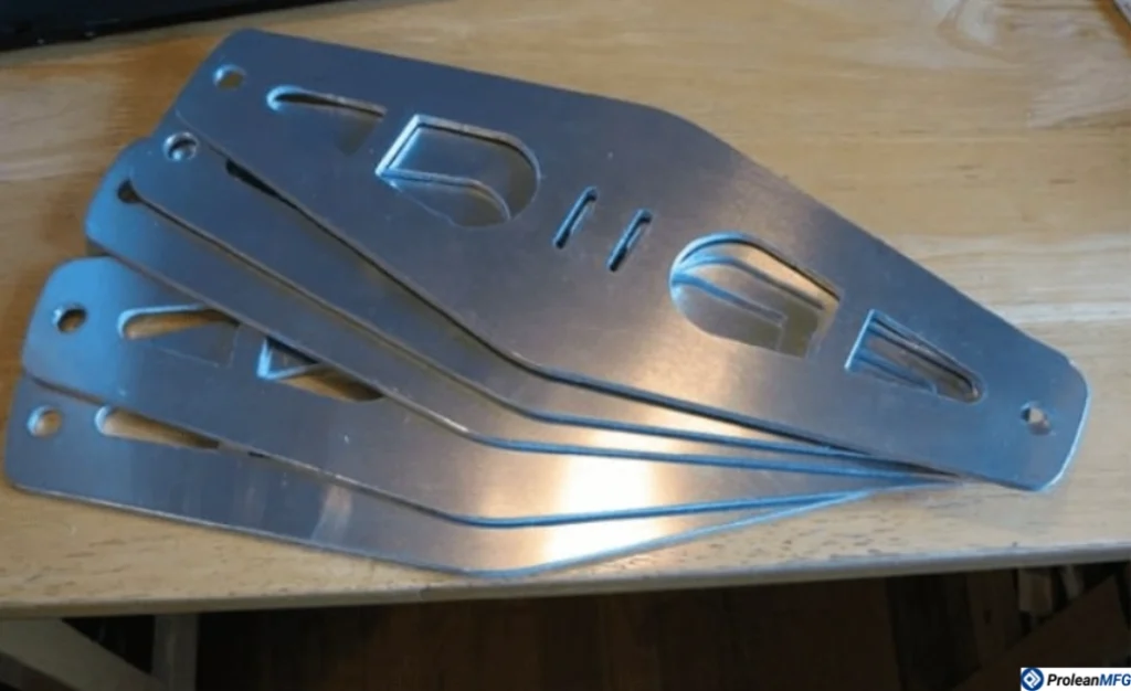 Five identical plasma-cut aluminum brackets on a wooden surface