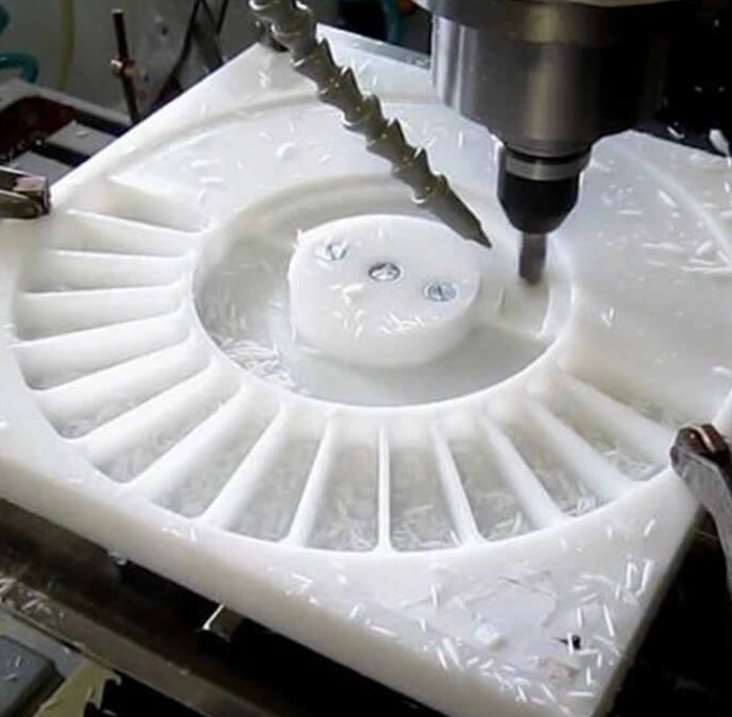 Square white polypropylene plate with round indentation being CNC machined with coolant.