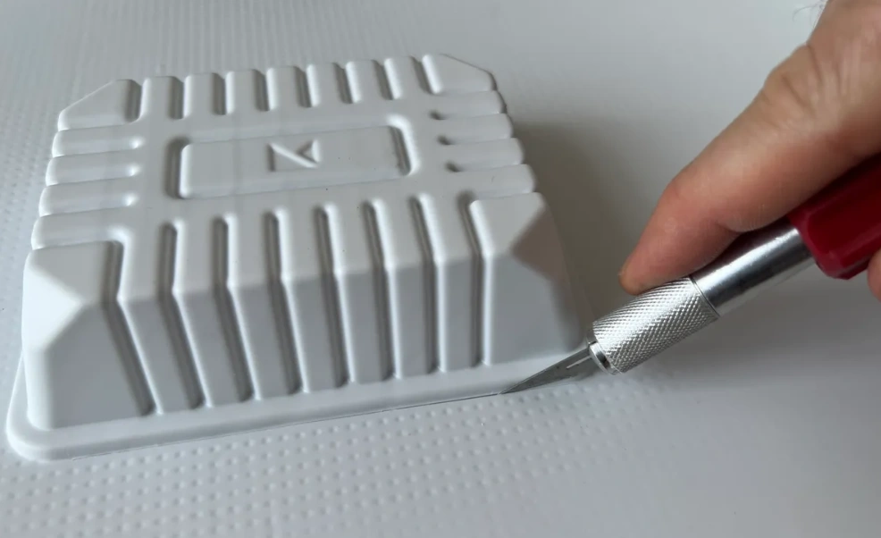 Thermoformed white plastic component with ribbed structure and fine detail features being trimmed