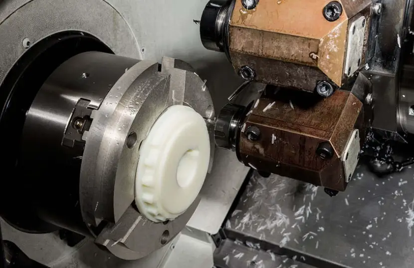 CNC lathe turning a white plastic part in a chuck with a cutting tool and chips