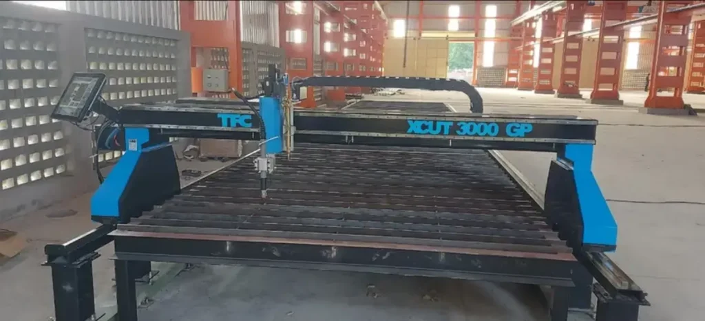 A CNC plasma cutting table with a gantry and control panel in an industrial workshop