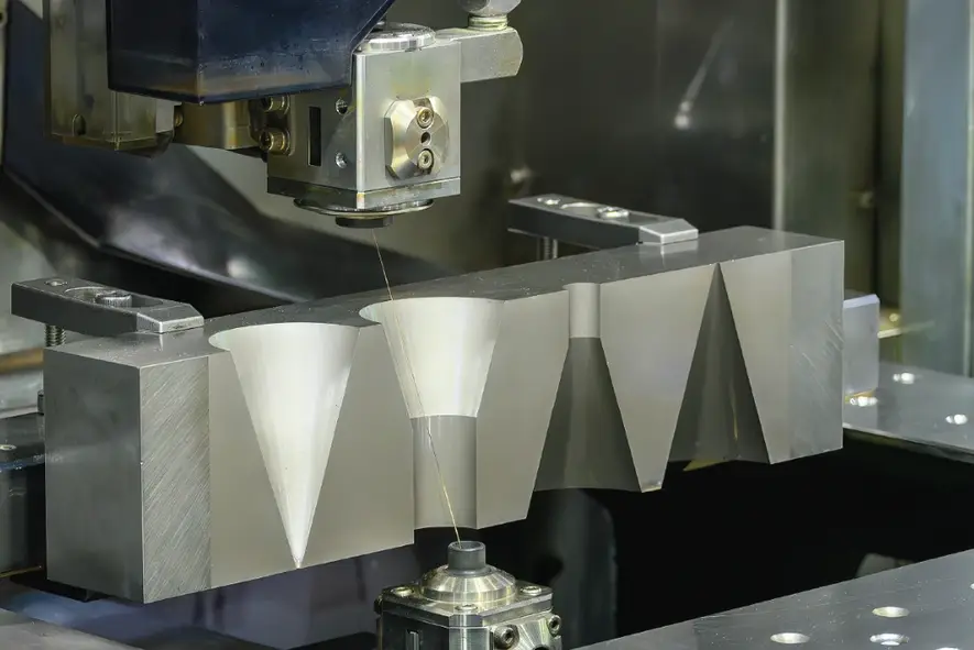 Wire EDM machine cutting precise conical profiles into an aerospace-grade metal block.   