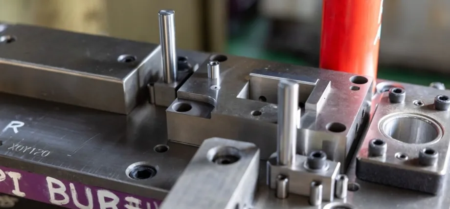 Detailed view of a precision metal stamping die with guide pins, punches, and engraved markings, mounted in a press tool setup.