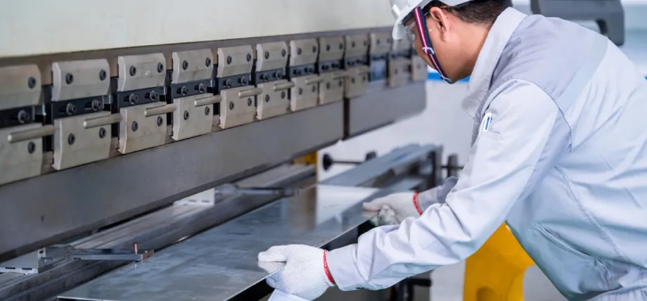 A flat metal sheet is fed into a CNC press brake machine for precision bending.