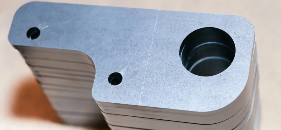 Close-up of a precision-machined aluminum L-bracket or mounting block with a large bored and countersunk circular hole, two smaller through-holes, and stacked identical parts