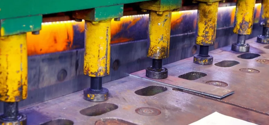 Close-up of a large industrial hydraulic press with yellow rams actively stamping a metal sheet on a perforated die bed