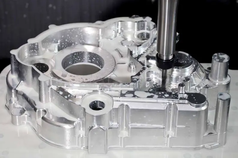 End mill machining a complex aluminum automotive engine housing with coolant fluid applied.