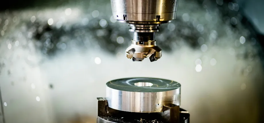 Precision CNC milling machine with a multi-flute end mill actively cutting a circular aluminum workpiece, producing fine metal chips