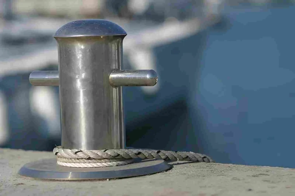 The image shows a shiny metal bollard installed on a pier, typically made from 316 stainless steel.