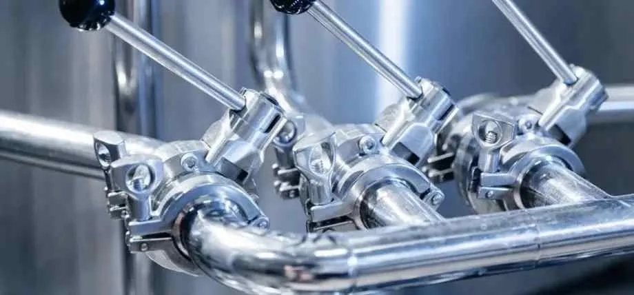 A complex network of polished stainless steel piping and industrial valves with manual control levers.