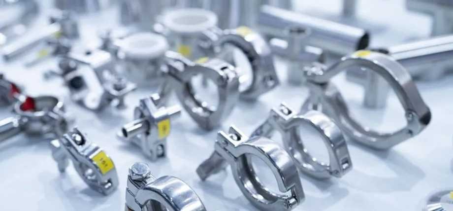 A wide variety of polished stainless steel pipe clamps and fittings are arranged on a white surface