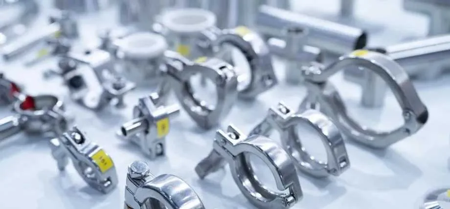 A wide variety of polished stainless steel pipe clamps and fittings are arranged on a white surface