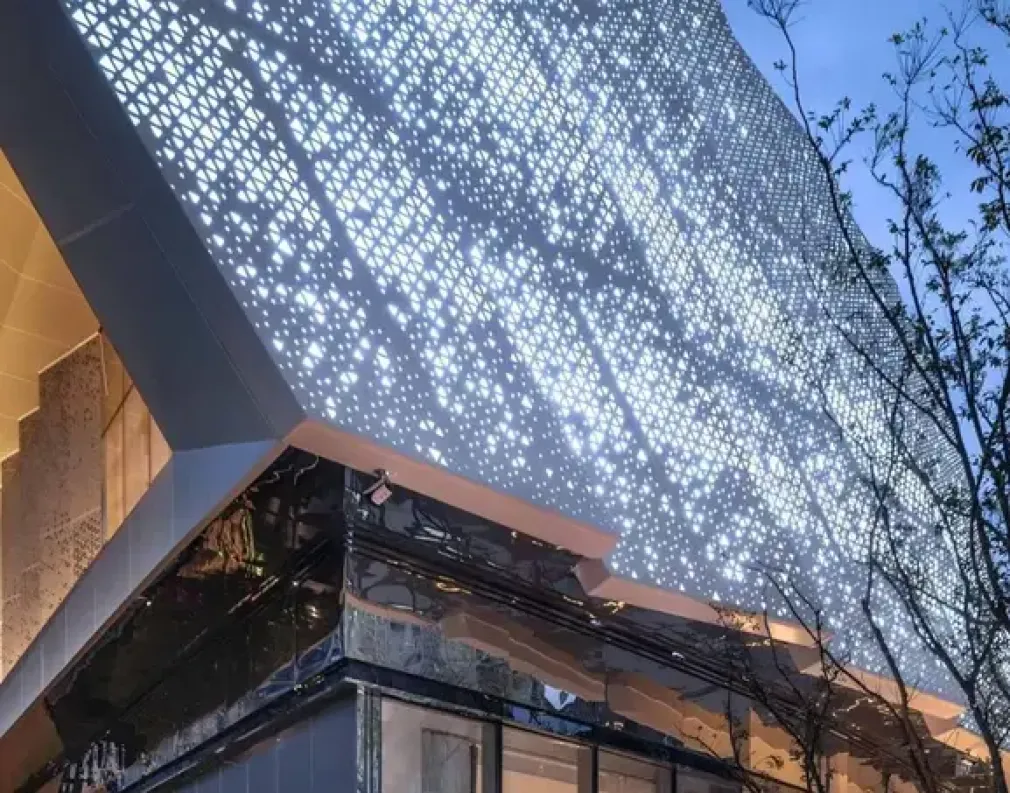 Architectural building facade clad in laser-cut aluminum panels with intricate geometric perforations, allowing light to filter through