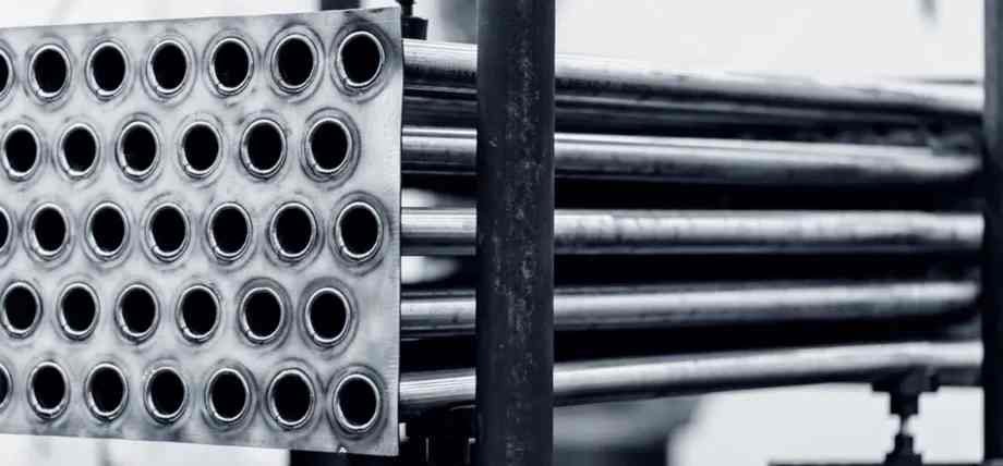 A close-up of a duplex stainless steel heat exchanger tube bundle secured by a thick metal plate.