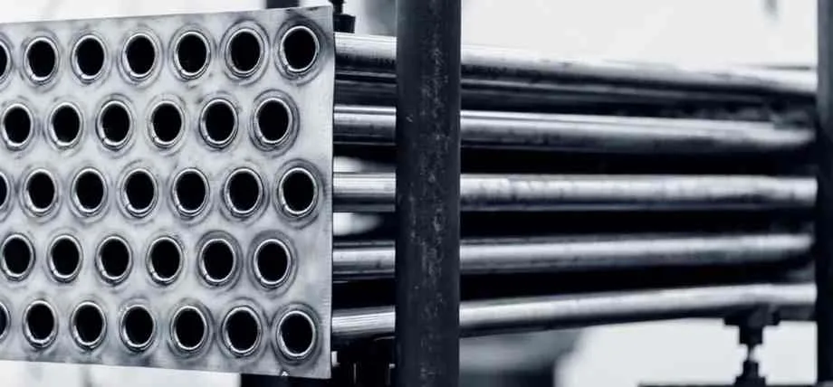 A close-up of a duplex stainless steel heat exchanger tube bundle secured by a thick metal plate.