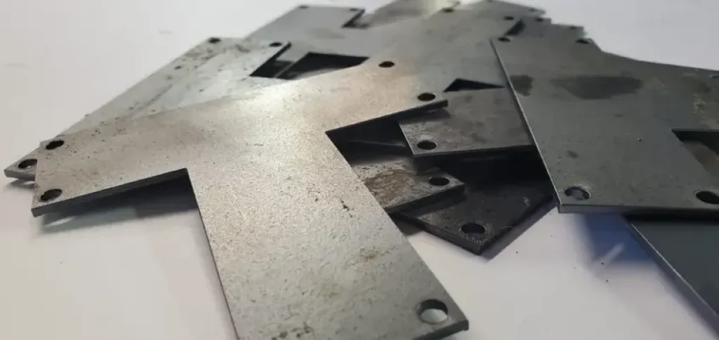Multiple flat laser cut aluminum sheets with precise holes and edges, stacked loosely on a white surface.