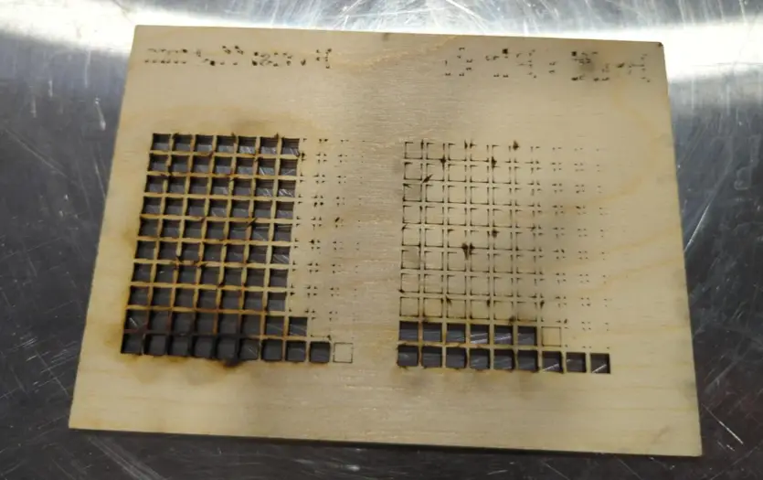 Laser-cut sheet with grid patterns showing burn marks and discoloration around cut edges