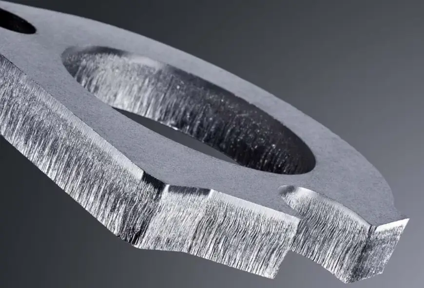 Close-up of a laser-cut stainless steel part showing rough, striated cut edges.