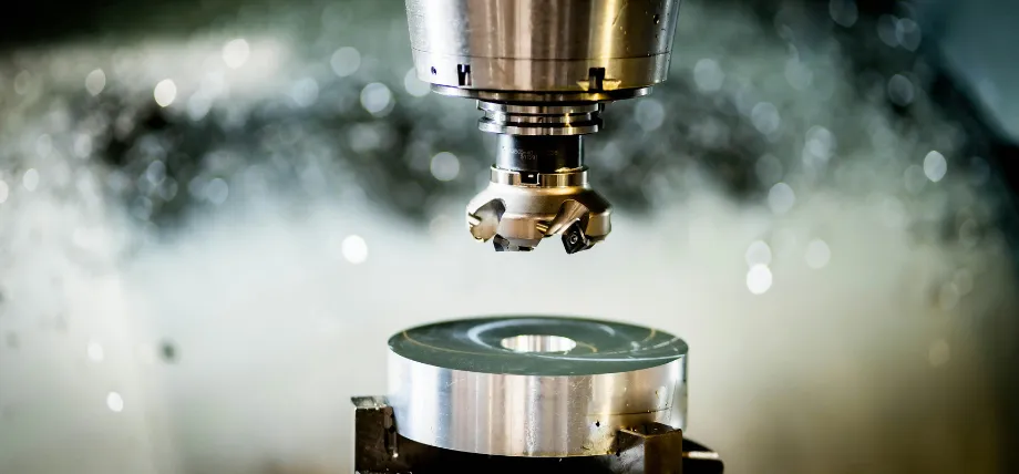 A CNC face mill cutting a circular steel workpiece with visible coolant mist and metal chips