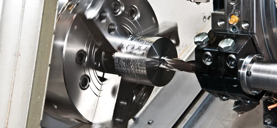 A lathe machine performing a turning operation on a cylindrical steel part with a drill bit engaged