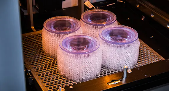 Four translucent resin cylinders freshly printed on a 3D printer build platform with support structures.