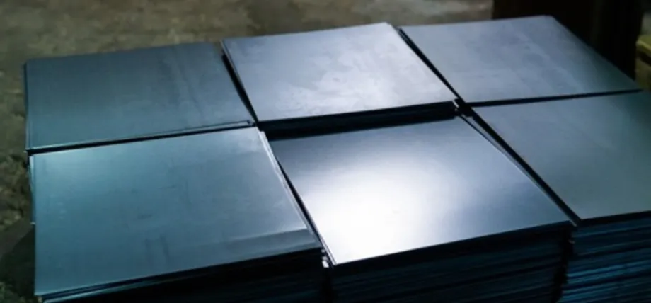 Neat stacks of square-cut dark grey metal sheets in an industrial setting