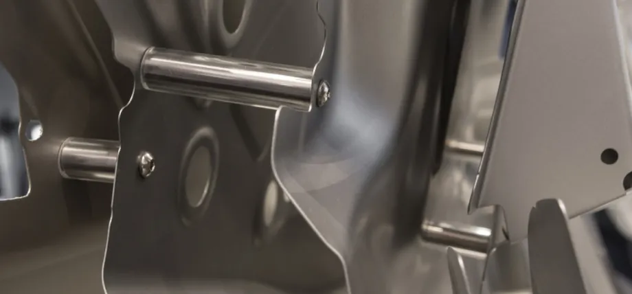 Close-up view of stainless steel sheet metal components featuring cylindrical rods secured with screws, assembled onto a curved bracket within a precision fabrication setup.