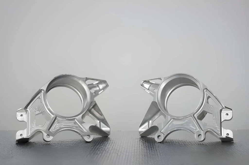 The image depicts an aluminum suspension upright, a component of a vehicle’s wheel assembly. The part has a machined surface with visible features such as mounting points and precise edges
