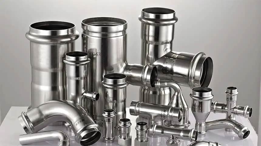 Assorted stainless steel pipe fittings, including elbows, tees, and couplings, are arranged on a white surface