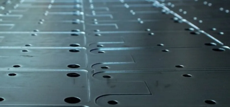 A perspective view of multiple identical rectangular metal parts laid out in a grid, showing precision-drilled holes and smooth machined edges.