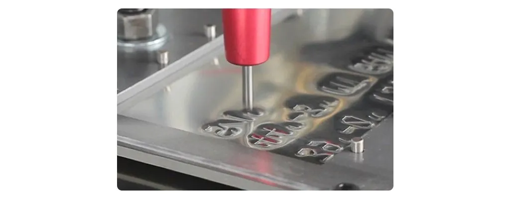 Close-up of a metal stamping machine pressing and embossing custom shapes into an aluminum sheet with a red tool head