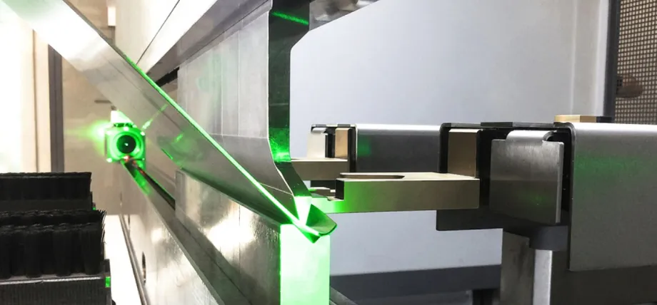 Close-up of a precision sheet metal bending operation on a press brake, illuminated by a vivid green laser alignment beam highlighting the bend line along the aluminum sheet.