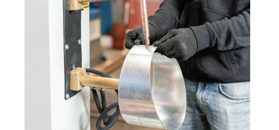manually feeding and forming a shiny sheet of aluminum into a cylindrical duct