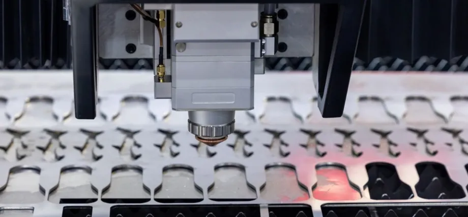 Close-up of a CNC laser cutting head with focused beam actively processing a sheet of metal, producing intricate patterns of nested parts