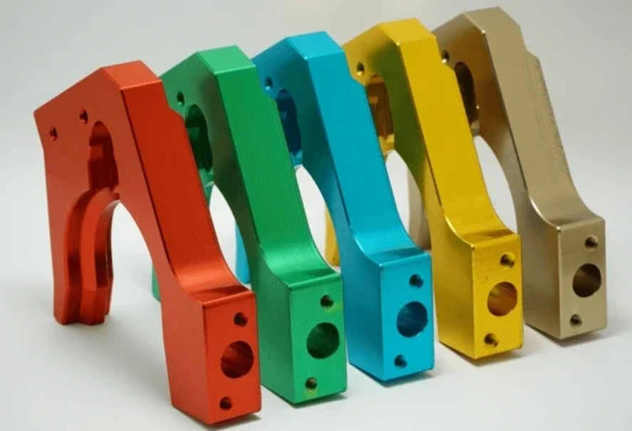 Five anodized aluminum CNC-machined brackets in red, green, teal, yellow, and gold finishes