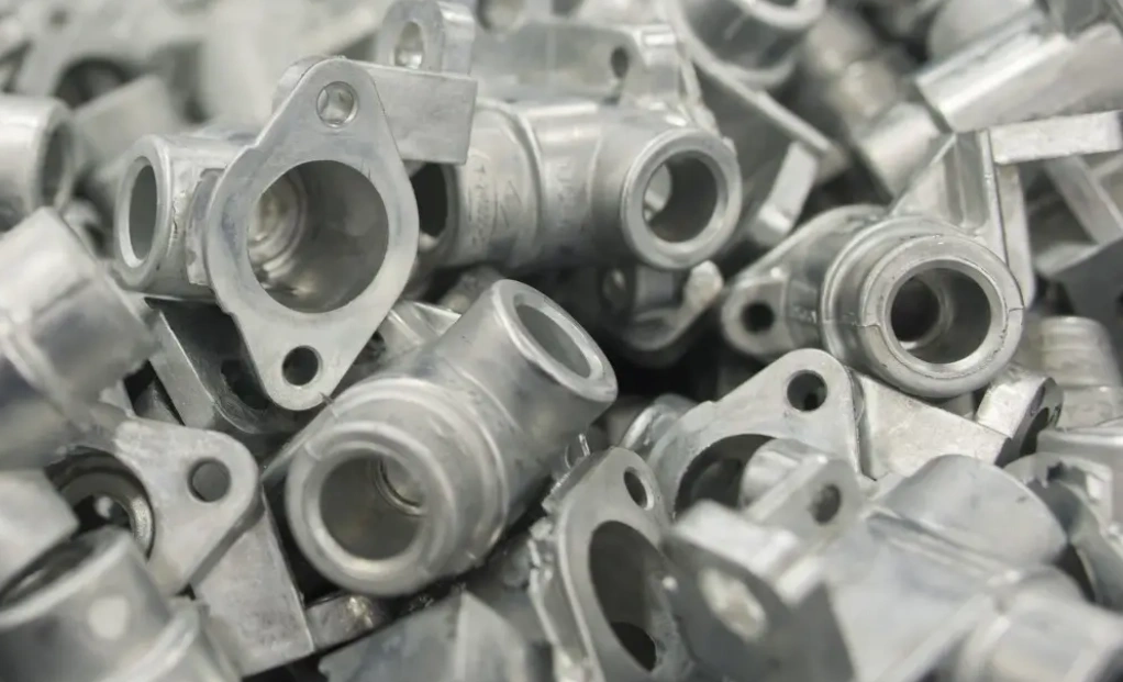 Pile of raw aluminum die-cast flanged pipe fitting parts in bulk production