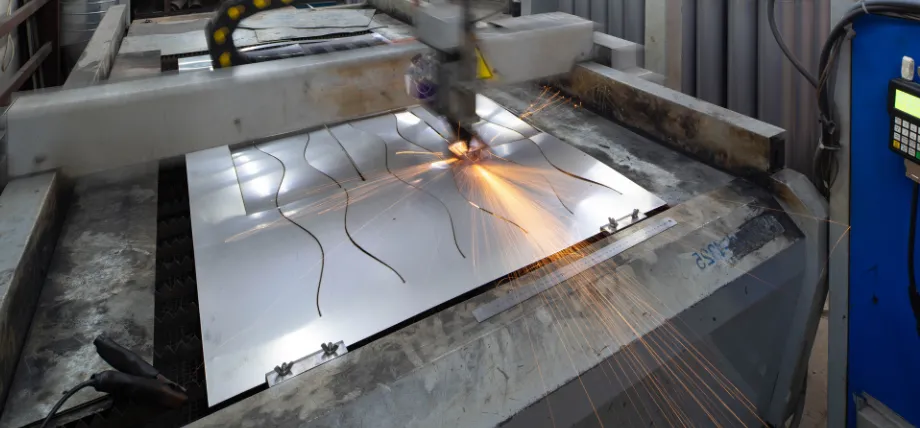 A CNC laser cutting machine processes an aluminum sheet, creating curved patterns with bright orange sparks flying from the contact point.