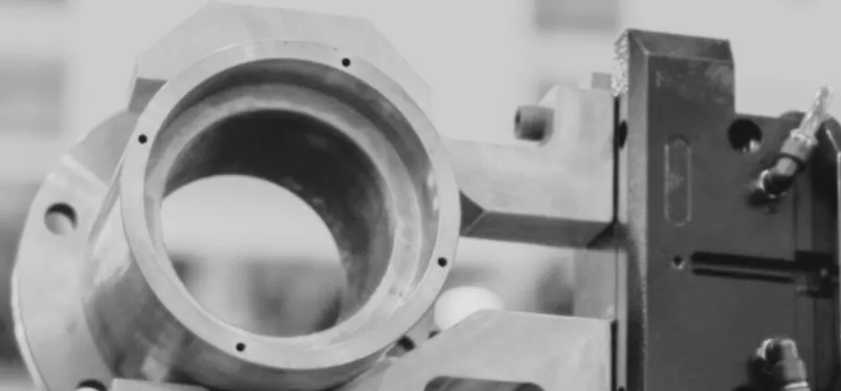 A heavy-duty metal CNC machining fixture holding a cylindrical part, shown in a grayscale industrial photo