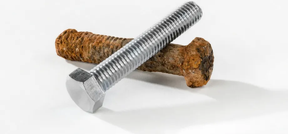 A clean, silver zinc-plated hex bolt resting on top of a heavily rusted and corroded brown iron bolt