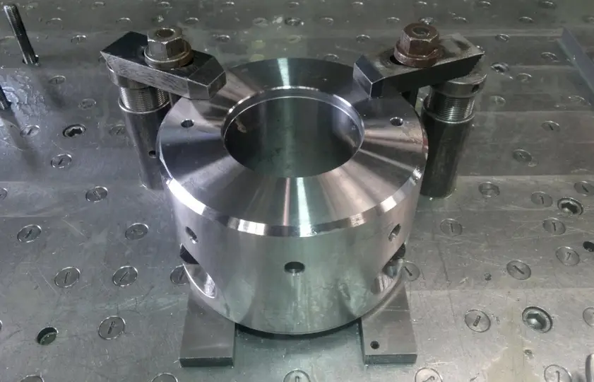 Polished CNC-machined aluminum marine flange part clamped on a metal worktable