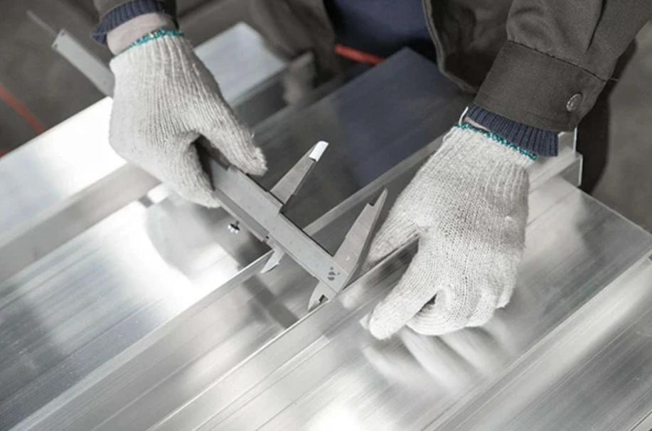 Gloved technician measuring a CNC-machined aluminum panel with a vernier caliper